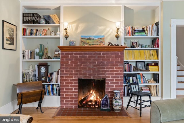 living room with hardwood / wood-style flooring, built in shelves, and a brick fireplace