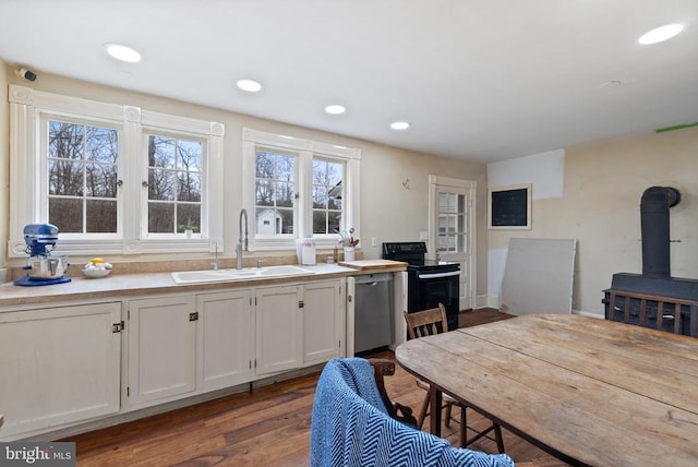 kitchen featuring sink, black electric range, white cabinets, stainless steel dishwasher, and a wood stove