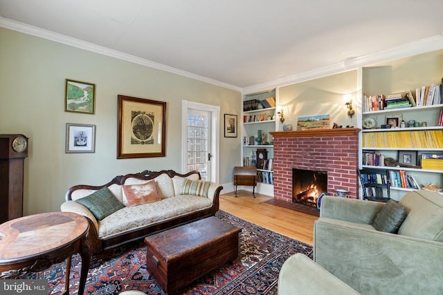 living room featuring hardwood / wood-style flooring, crown molding, built in shelves, and a brick fireplace