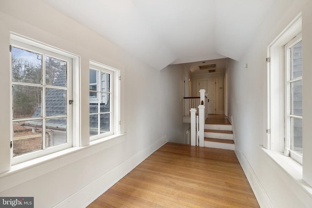 corridor with lofted ceiling, light hardwood / wood-style floors, and a healthy amount of sunlight