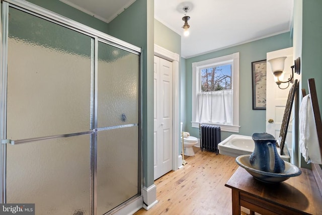 bathroom with radiator heating unit, wood-type flooring, ornamental molding, an enclosed shower, and toilet