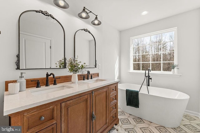 bathroom with double vanity, a freestanding tub, recessed lighting, and a sink