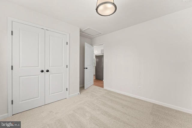 unfurnished bedroom featuring a closet, attic access, baseboards, and carpet floors