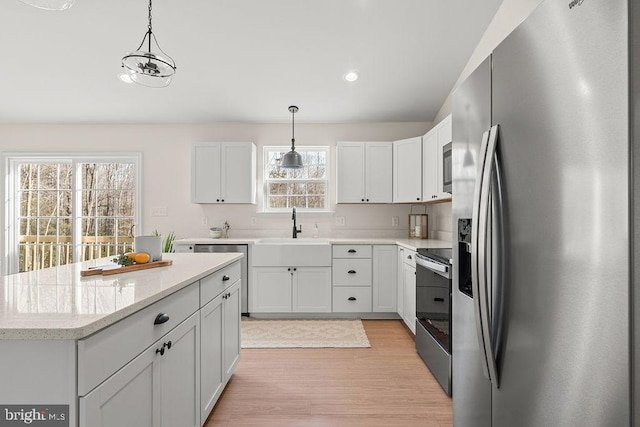 kitchen featuring light wood-style flooring, a sink, hanging light fixtures, appliances with stainless steel finishes, and a center island