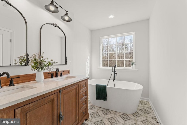 bathroom with a soaking tub, double vanity, baseboards, and a sink