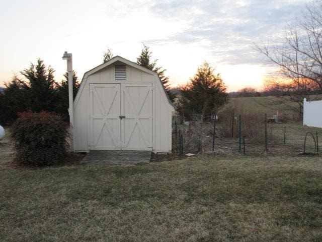 outdoor structure at dusk with a storage unit, a lawn, and an outbuilding