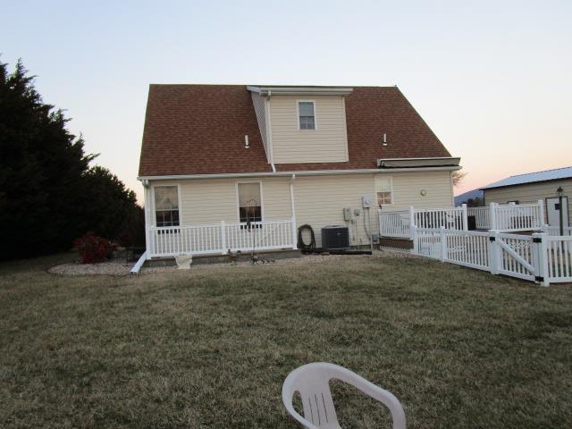 back of property at dusk featuring a gate, a lawn, central AC unit, and fence