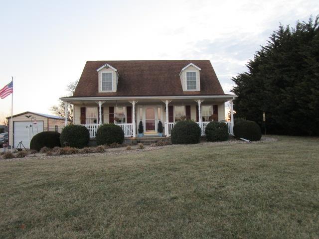 cape cod house with covered porch, a front yard, an outbuilding, and a garage