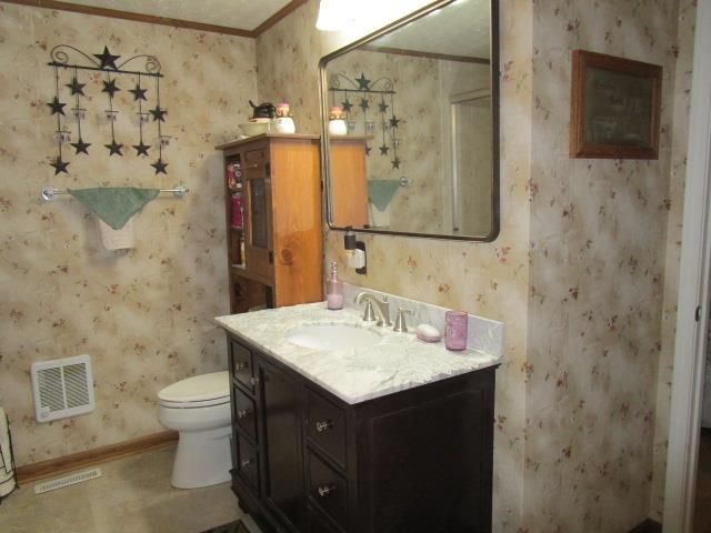 bathroom featuring visible vents, vanity, toilet, and wallpapered walls