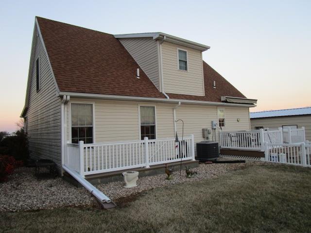 back of property at dusk featuring roof with shingles, central AC unit, a lawn, and a wooden deck