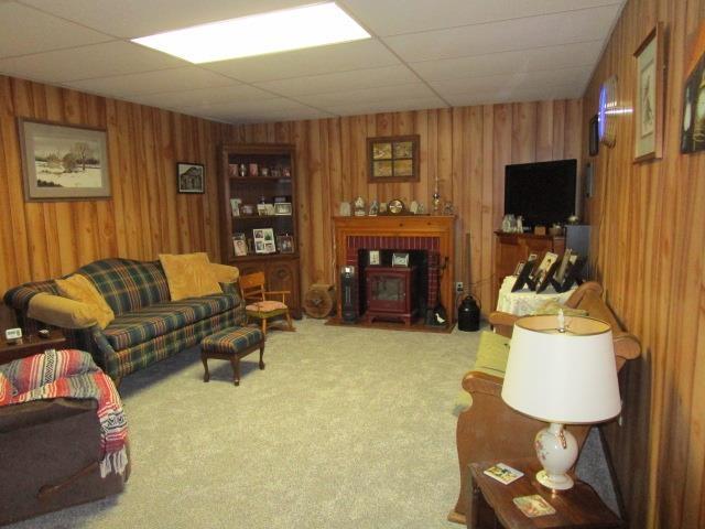 carpeted living area with a drop ceiling and wood walls