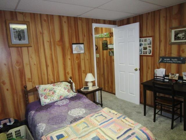 carpeted bedroom featuring a paneled ceiling and wood walls