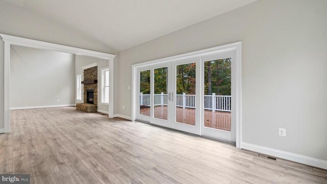 unfurnished living room with vaulted ceiling, a fireplace, and light wood-type flooring