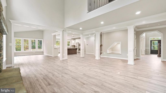 unfurnished living room featuring decorative columns, crown molding, a towering ceiling, and light hardwood / wood-style flooring