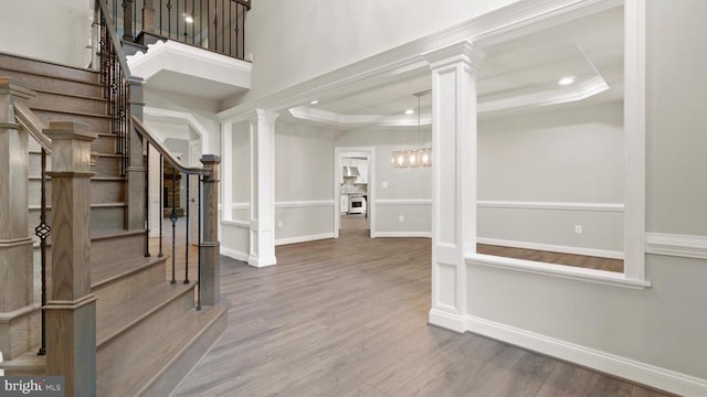 entryway with decorative columns, wood-type flooring, and a tray ceiling