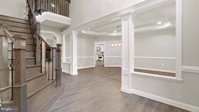 entryway with decorative columns, wood-type flooring, and a tray ceiling