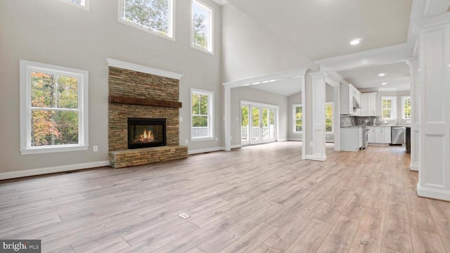 unfurnished living room with a towering ceiling, a fireplace, decorative columns, and light wood-type flooring