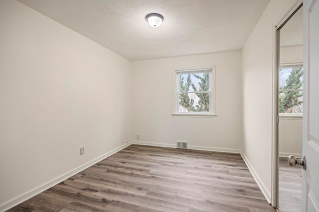 empty room with a healthy amount of sunlight, a textured ceiling, and light hardwood / wood-style floors