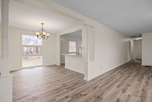 unfurnished dining area featuring a chandelier, decorative columns, light hardwood / wood-style flooring, and a textured ceiling