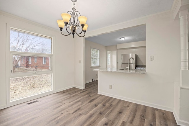 unfurnished dining area with sink, a notable chandelier, ornamental molding, and hardwood / wood-style floors