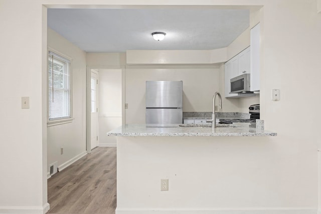 kitchen featuring stainless steel appliances, sink, light stone counters, and kitchen peninsula