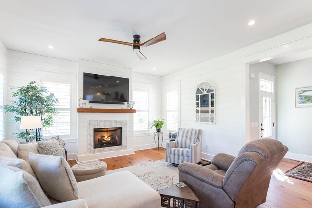 living room with a tiled fireplace, light hardwood / wood-style flooring, and ceiling fan