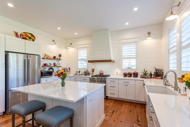 kitchen featuring a kitchen bar, wall chimney exhaust hood, sink, high end appliances, and white cabinetry