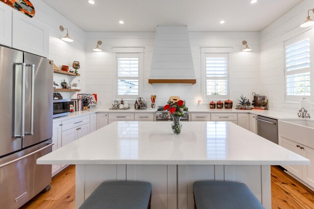 kitchen with wall chimney range hood, a kitchen breakfast bar, a kitchen island, stainless steel appliances, and white cabinets