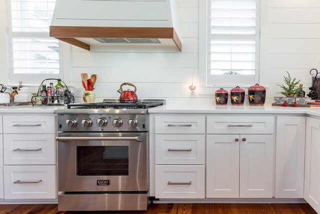 kitchen with stainless steel stove, custom range hood, and white cabinets