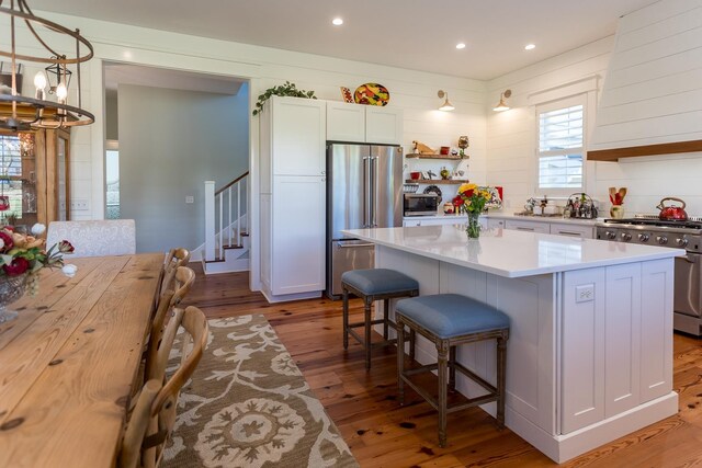 kitchen featuring white cabinetry, hanging light fixtures, high quality appliances, a kitchen island, and light hardwood / wood-style floors