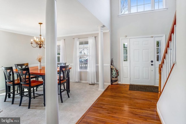 carpeted entrance foyer with wood finished floors, a healthy amount of sunlight, a chandelier, and crown molding