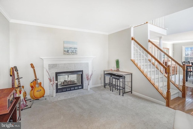 carpeted living area featuring ornamental molding, decorative columns, a premium fireplace, baseboards, and stairs