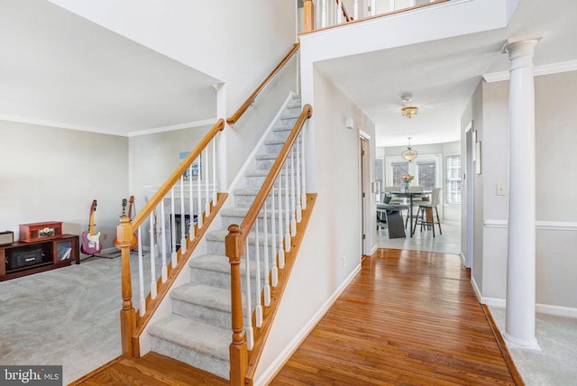 stairway featuring a ceiling fan, wood finished floors, baseboards, decorative columns, and crown molding