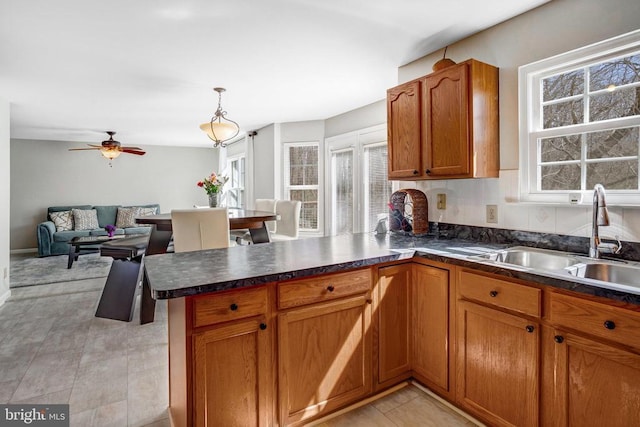 kitchen featuring dark countertops, a peninsula, brown cabinetry, a ceiling fan, and a sink