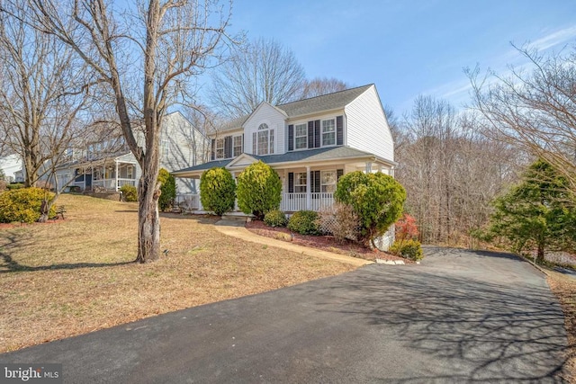 view of front of house featuring covered porch, driveway, a front lawn, and roof with shingles