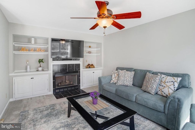 carpeted living room with a tiled fireplace, built in features, baseboards, and ceiling fan