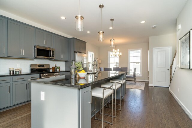 kitchen with pendant lighting, backsplash, stainless steel appliances, and a center island with sink