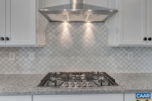 kitchen featuring white cabinetry, decorative backsplash, stainless steel gas cooktop, light stone countertops, and wall chimney exhaust hood