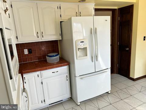 kitchen with white cabinetry, tile countertops, white refrigerator with ice dispenser, and tasteful backsplash