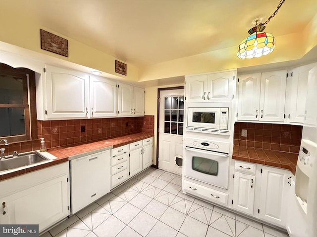 kitchen featuring tile countertops, decorative backsplash, white cabinets, white appliances, and a sink