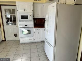 kitchen with white appliances, light tile patterned flooring, and white cabinetry