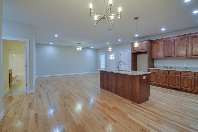 kitchen with light wood finished floors, a sink, recessed lighting, pendant lighting, and light stone counters