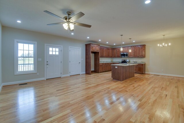 kitchen with light wood-style floors, brown cabinetry, a kitchen island, and appliances with stainless steel finishes