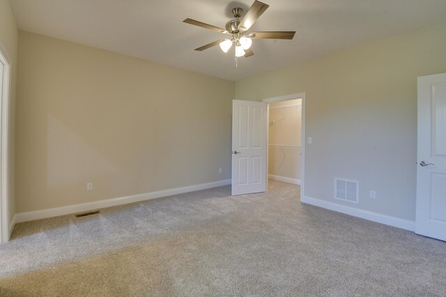 unfurnished bedroom with light colored carpet, a walk in closet, visible vents, and a closet