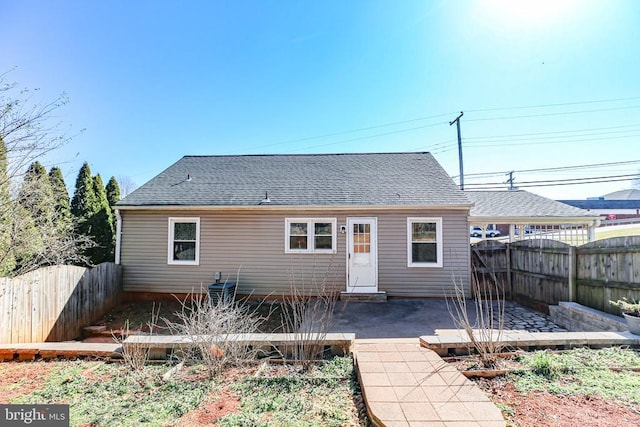 rear view of property with a patio, roof with shingles, and a fenced backyard