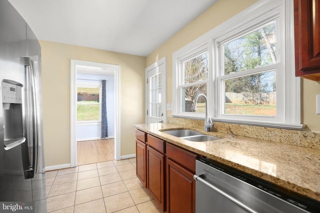 kitchen featuring light stone counters, light tile patterned floors, baseboards, a sink, and appliances with stainless steel finishes