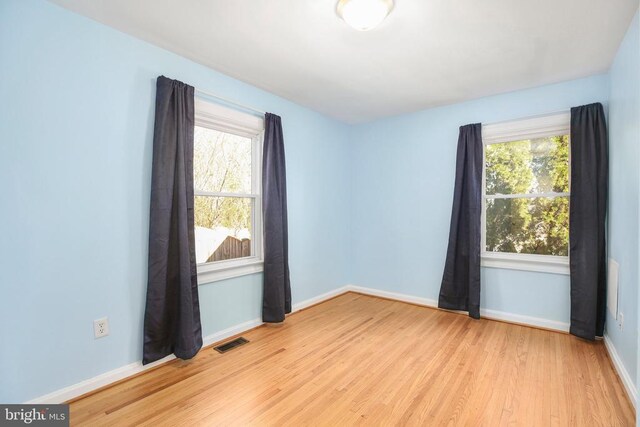 unfurnished room with a wealth of natural light, visible vents, baseboards, and wood finished floors