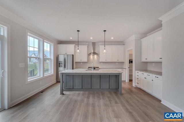 kitchen featuring stainless steel fridge, an island with sink, pendant lighting, light stone countertops, and wall chimney range hood