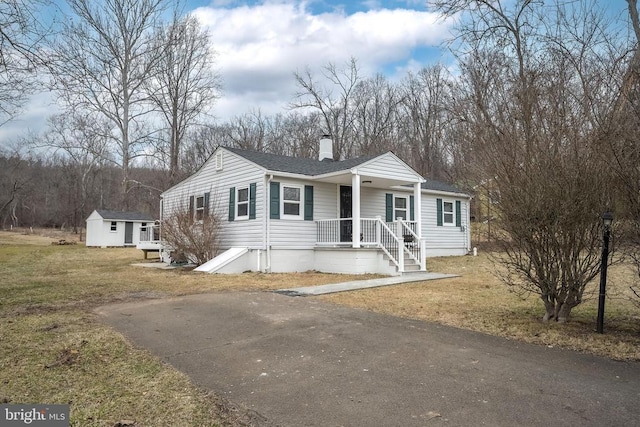 view of front of property featuring aphalt driveway, an outbuilding, a chimney, a storage unit, and a front lawn