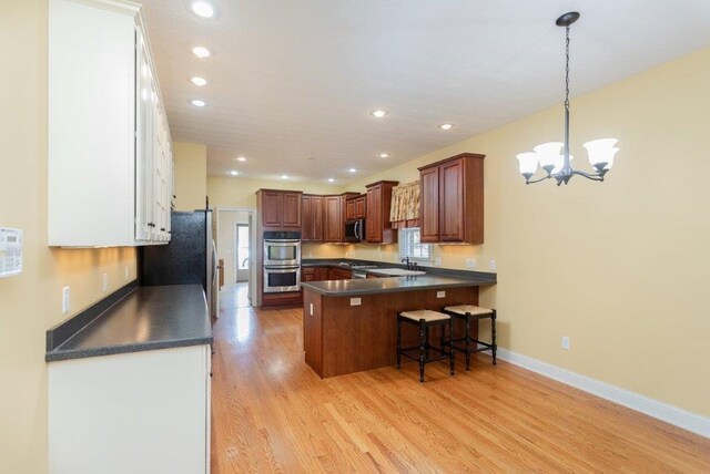 kitchen with appliances with stainless steel finishes, a breakfast bar, decorative light fixtures, kitchen peninsula, and light hardwood / wood-style flooring